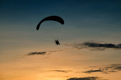 Low angle view of person paragliding against sky during sunset