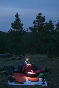 Woman writing on book while camping on field at dusk