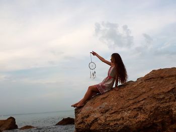 Woman sitting on rock by sea against sky