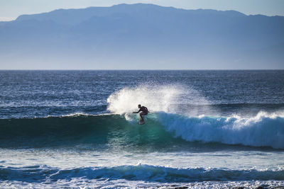 Silhouette teenage boy surfing in sea against mountains