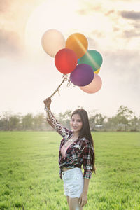 Portrait of young woman with balloons on field