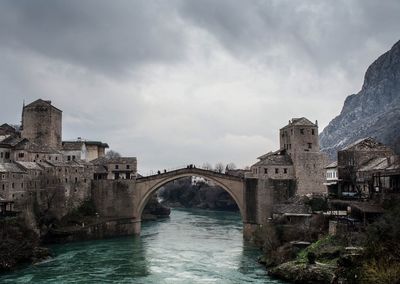 Arch bridge over river against cloudy sky