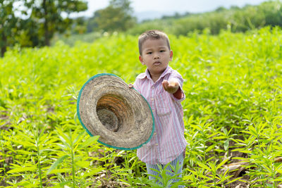 Portrait of boy holding hat while standing on field