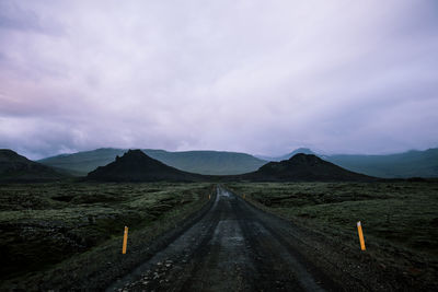 Empty road leading towards mountains against sky