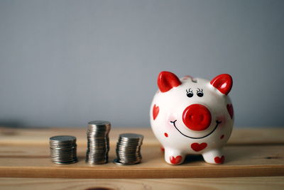Close-up of coins with piggy bank on table against wall