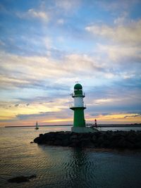 Lighthouse by sea against sky during sunset