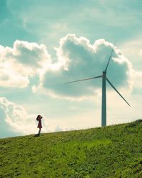 Rear view of man standing on field against sky, holding umbrella, beside a windmill