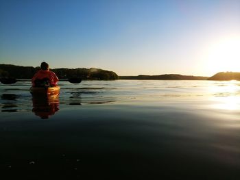 Rear view of man on shore against sky during sunset