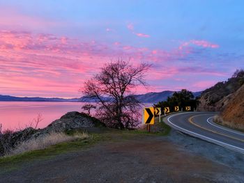 Road by trees against sky during sunset