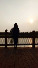 Rear view of man on footbridge over river against sky during sunset