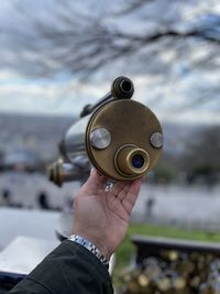 Close-up of hand holding metal scope against sky