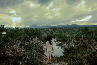 Rear view of woman standing on field against cloudy sky during sunset