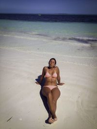 Full length of woman wearing bikini relaxing at beach on sunny day