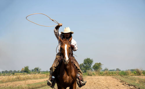 Man holding noose while riding on horse against sky