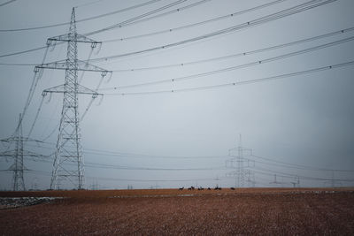 Low angle view of electricity pylon on field with wild deer against sky