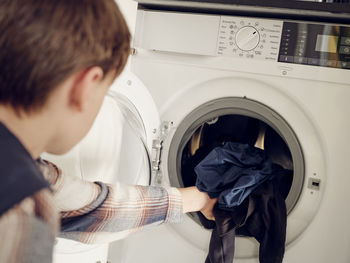 Boy putting laundry into washing machine at home