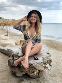 Young woman sitting on rock at beach against sky