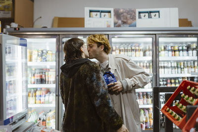 Affectionate young gay couple kissing while standing at aisle in supermarket