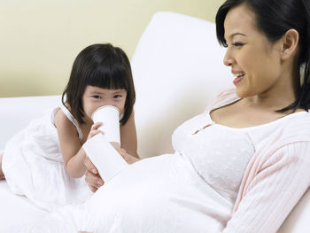 Girl speaking pregnant mother abdomen with tin can phone on sofa