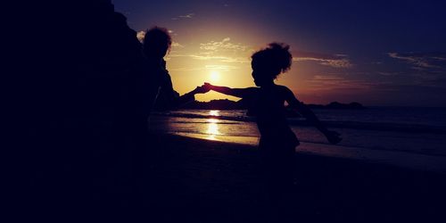 Silhouette woman standing on beach against sky during sunset