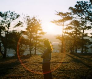 Side view of woman standing on field against sky during sunset