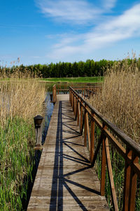 Wooden footbridge on field against sky