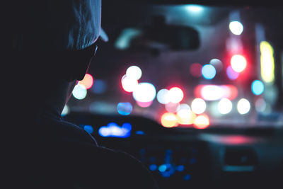 Rear view of man driving car against illuminated city at night
