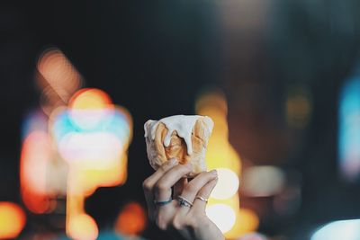 Cropped hand of woman holding sweet food against illuminated lights at night