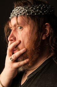 Profile view of mid adult man with beard wearing chains on head against black background