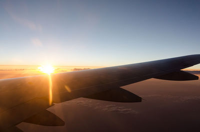 Airplane wing against sky during sunset