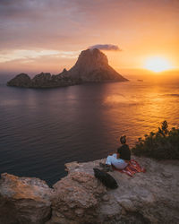 Woman sitting against sea during sunset