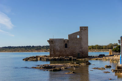 Old building by lake against blue sky