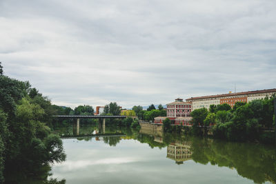 Arch bridge over river by buildings against sky