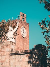 Low angle view of statue and clock tower against clear blue sky