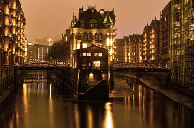 Bridge over river amidst buildings in city at night