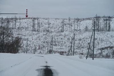 Snow covered road amidst trees against sky