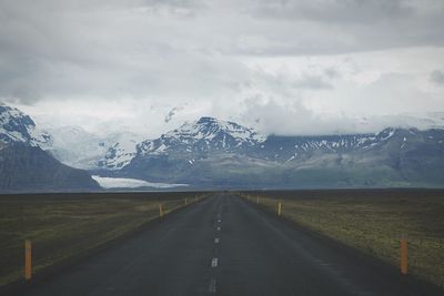 Road leading towards snowcapped mountains against cloudy sky