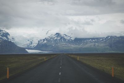 Road passing through snow covered mountains against cloudy sky