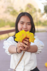 Portrait of woman holding yellow while standing outdoors