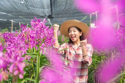 Portrait of woman celebrating while standing amidst plants in greenhouse