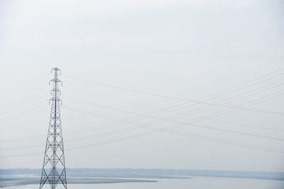 Electricity pylon by sea against clear sky