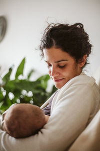 Close-up of smiling mid adult woman breastfeeding newborn girl at home