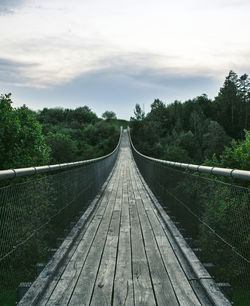 Footbridge amidst trees in forest against sky