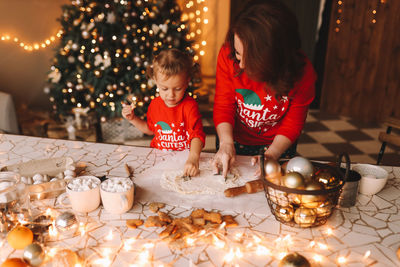 Parents and a child in red pajamas prepare christmas cookies in the decorated kitchen of the house