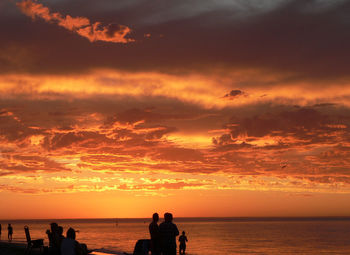 Silhouette people on beach against sky during sunset