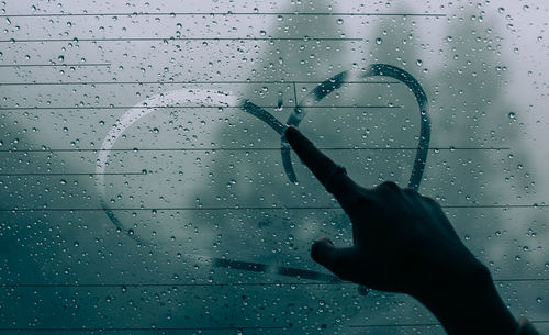 Cropped image of person drawing heart shape on wet glass