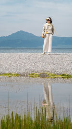 Rear view of woman standing at beach against sky