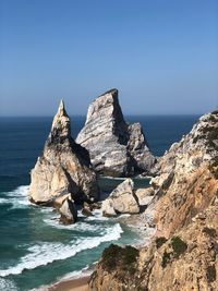 Scenic view of rocks in sea against clear blue sky