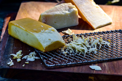 Smoked cheese block partially grated on vintage metal cheese grater on wood cutting board