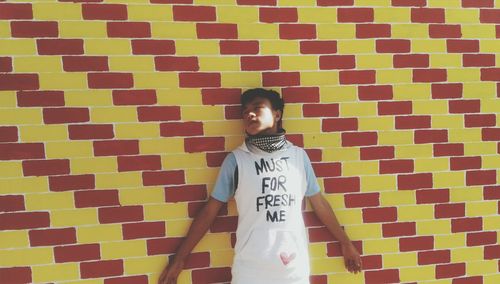 Man with text on t-shirt standing against brick wall